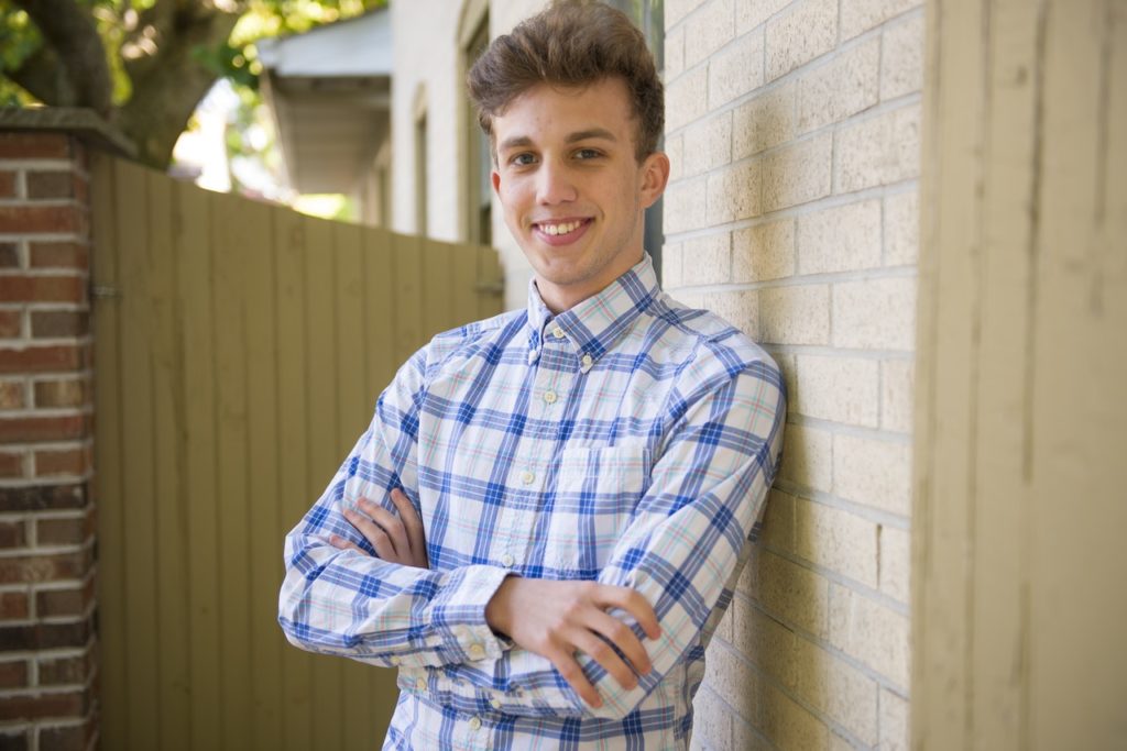 Smiling young man in plaid shirt standing against brick wall in backyard